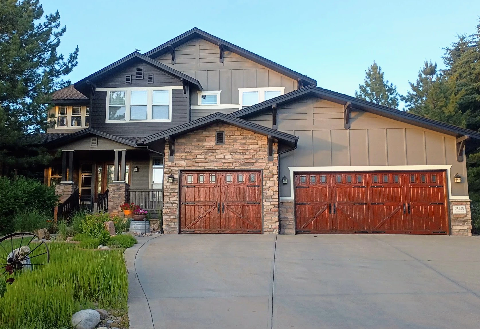 Large craftsman-style home exterior with stone accents, wood garage doors, and dark trim