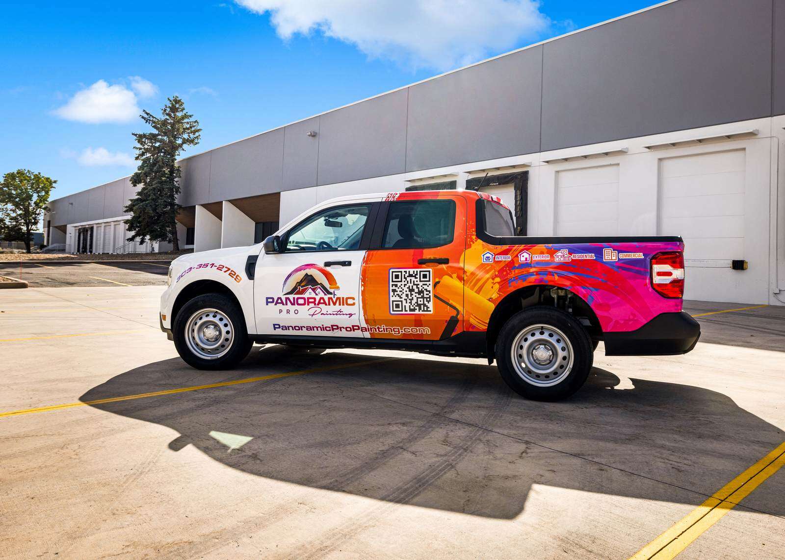 Panoramic Pro Painting wrapped work truck parked in front of a gray and white commercial building, side view showing interior, exterior, residential, and commercial service icons