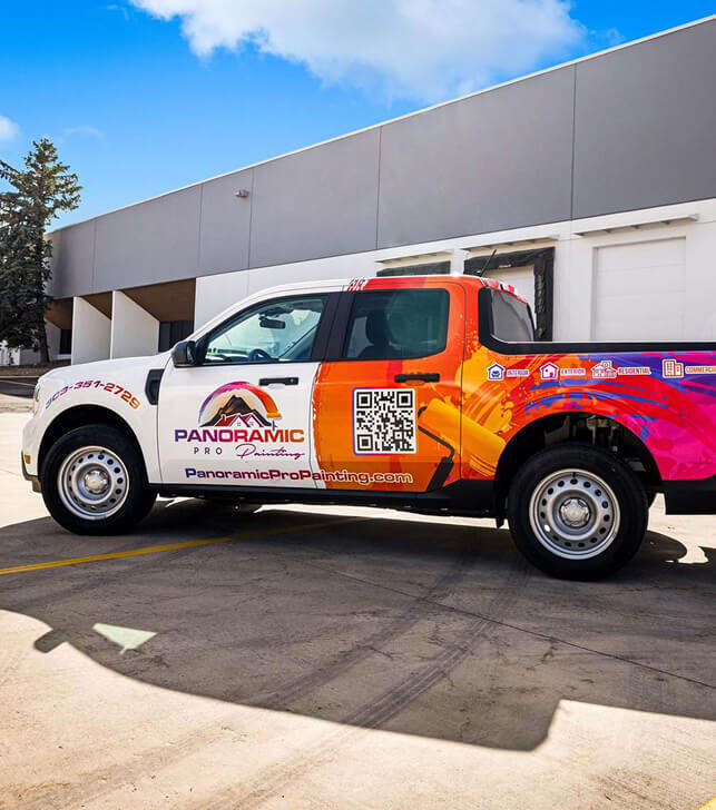 Panoramic Pro Painting wrapped work truck parked in front of a gray and white commercial building, side view showing interior, exterior, residential, and commercial service icons